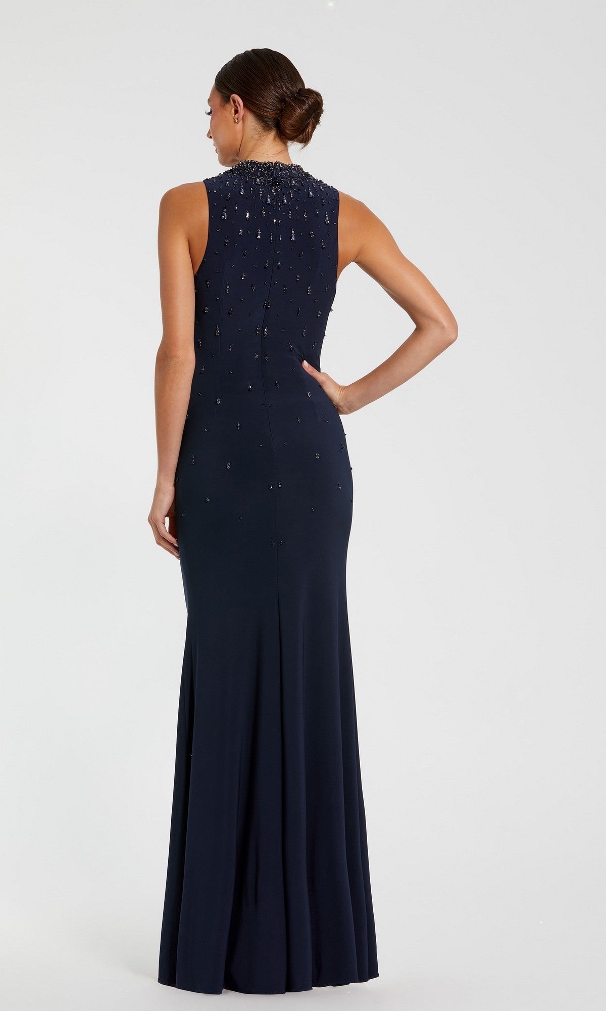 Woman in a sleeveless, floor-length black Mac Duggal 2260 high-neck formal gown with beaded embellishments on the upper back stands with her back to the camera.